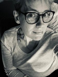 A black and white photo of refuge volunteer Becky. She is looking up into the camera and is wearing glasses and appears ready to listen